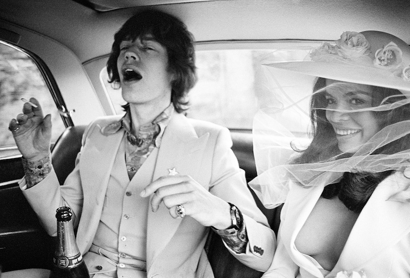 Mick and Bianca Jagger, wearing suits in the back of their wedding car.