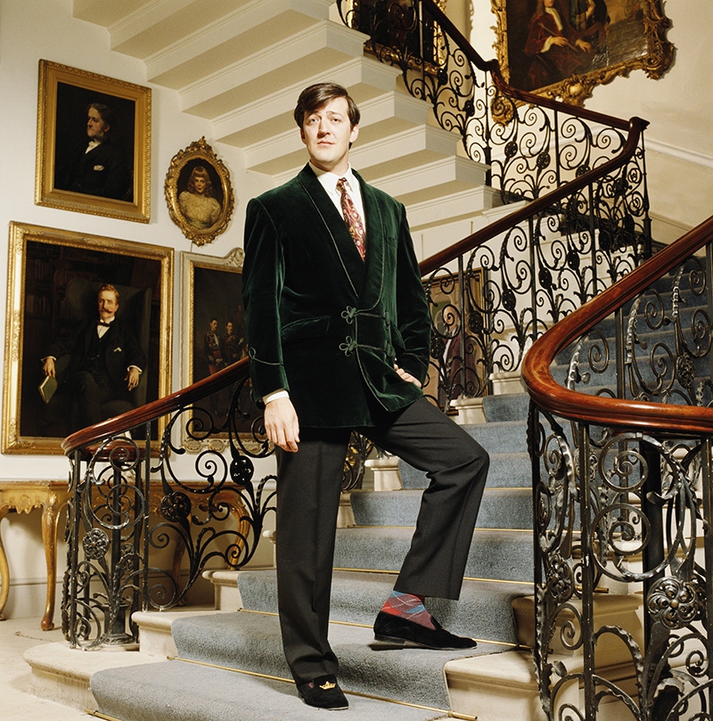 English comedian Stephen Fry looking rakish in a lounge coat and velvet slippers.