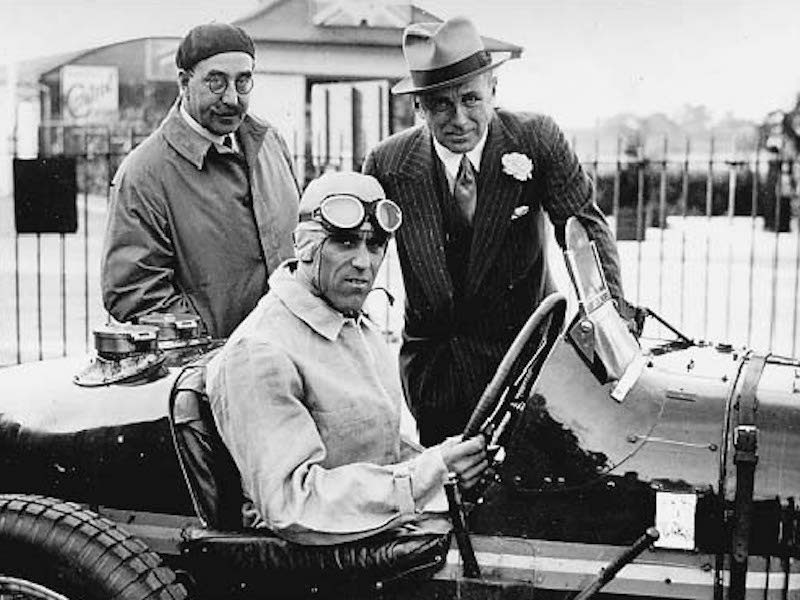 Tazio Nuvolari sits in the Earl of Howe's Bugatti while the dapper Earllooks on, accompanied by  Hugh McConnell