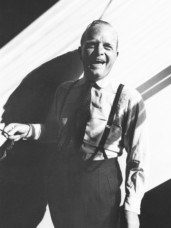 Writer Truman Capote standing in a sunbeam, laughing, dressed in a striped dress shirt, tie and pants with suspenders, 1965. Image by © Condé Nast Archive/Corbis.