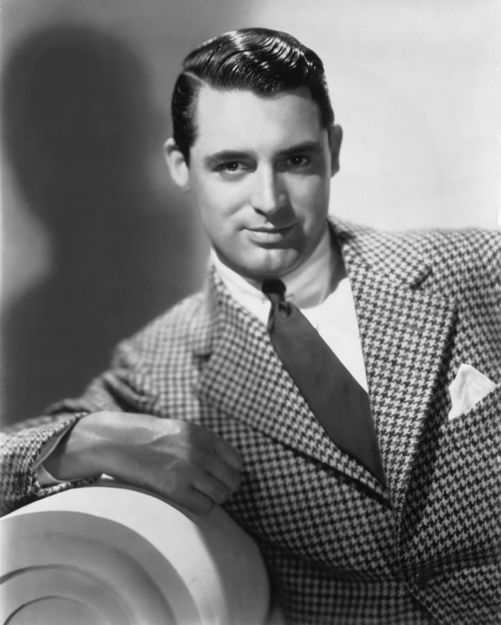 A young Cary Grant in a double-breasted tweed Prince of Wales glenplaid sportcoat and rectangular dress watch.