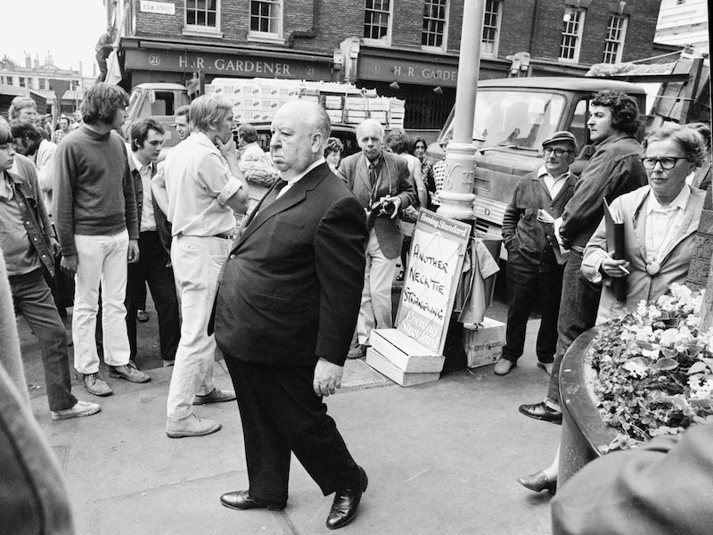 English film director Alfred Hitchcock during location filming in Covent Garden, London, for his film 'Frenzy', 1971. The set is dressed with a newspaper sign (right) reading: 'Another Necktie Strangling'. Photo by Jack Kay/Daily Express/Hulton Archive/Getty Images.