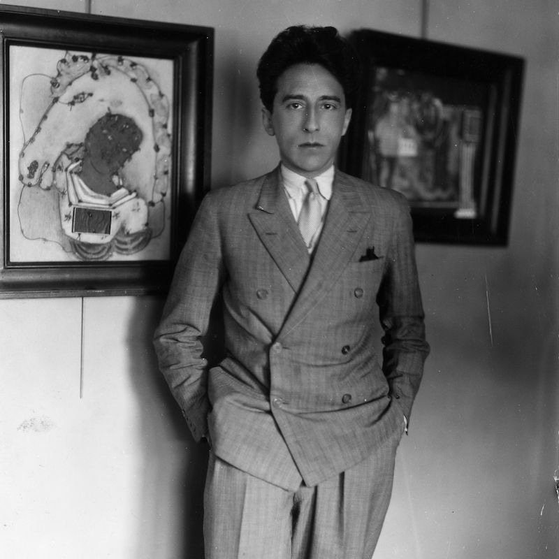 Jean Cocteau standing next to one of his paintings (left). Photo by Sasha/Getty Images.