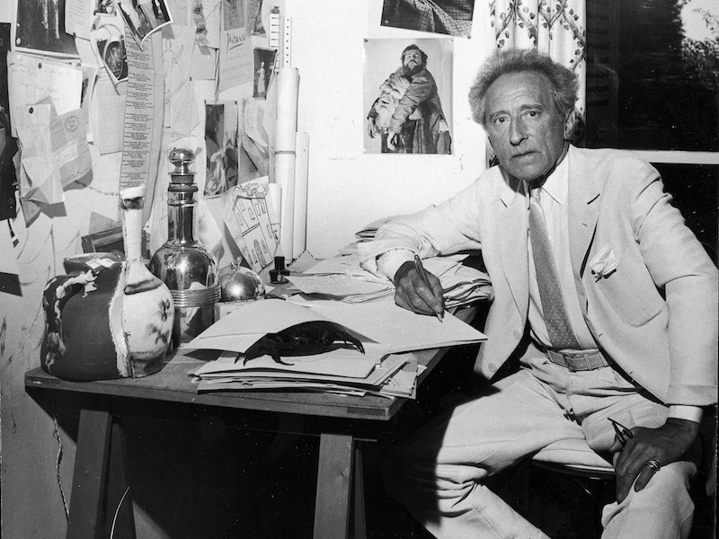 Jean Cocteau sitting at a desk. The wall holds many clippings belonging to American friend Francine Weisweller, where he was living. Photo by Leo Rosenthal/Pix Inc./The LIFE Images Collection/Getty Images.