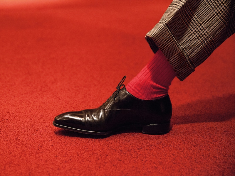 While his suits tend to be sober, he injects color with his socks. He has an appreciation for shoes but keeps it simple with a bench-made cap toe here. Anchoring the look to the ground are highly polished and elegant Oxfords from British shoemakers Gaziano & Girling.