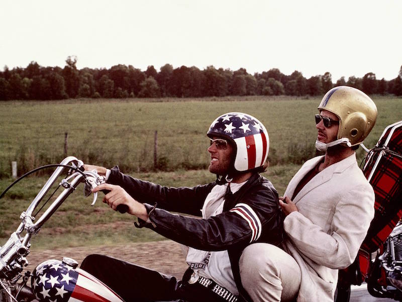 Peter Fonda, wearng a stars-and-stripes helmet, and Jack Nicholson, wearing a gold American football helmet, as they ride Fonda's chopper motorcycle in a publicity still issued for the film, 'Easy Rider', USA, 1969. Photo by Silver Screen Collection/Getty Images.