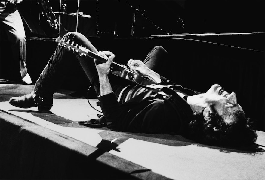 Rock and roll icon Bruce Springsteen falls to the stage and continues playing the guitar on his back during a 1979 Los Angeles, California concert at the Sports Arena. Springsteen spent much of 1978 playing small midwest venues while he battled his record label over control of his music. Photo by George Rose/Getty Images.