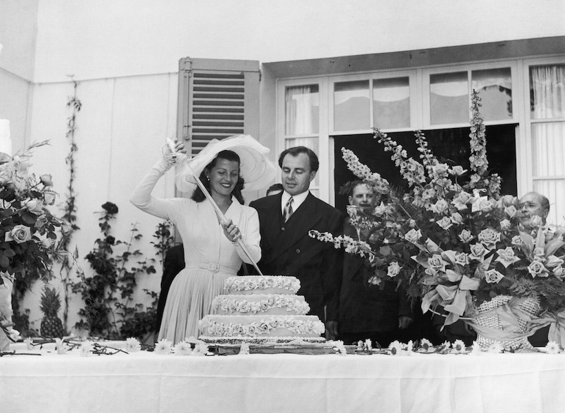 Prince Aly Khan watching bride, actress Rita Hayworth cutting into their wedding cake with a glass sword at Khan's Riviera Chateau de L'Horizon. Photo by Nat Farbman/The LIFE Picture Collection/Getty Images.
