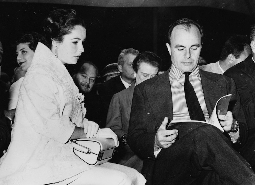 Prince Aly Khan reading the item catalogue, sitting next to actress Elizabeth Taylor, at an auction of his paintings in Paris, May 23rd 1957. Photo by Keystone/Hulton Archive/Getty Images.