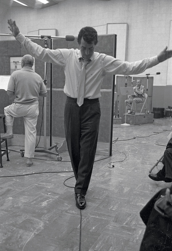 During a recording session, American actor and musician Dean Martin 'balances' on a straw power cord as he clowns about in a studio, Los Angeles, California, 1958. Photo by Allan Grant/The LIFE Picture Collection/Getty Images.