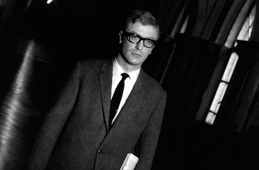 Caine in The Ipcress File in 1965, wearing a slightly looser cut suit than usual yet with his signature horn-rimmed glasses and somewhat vacant gaze.