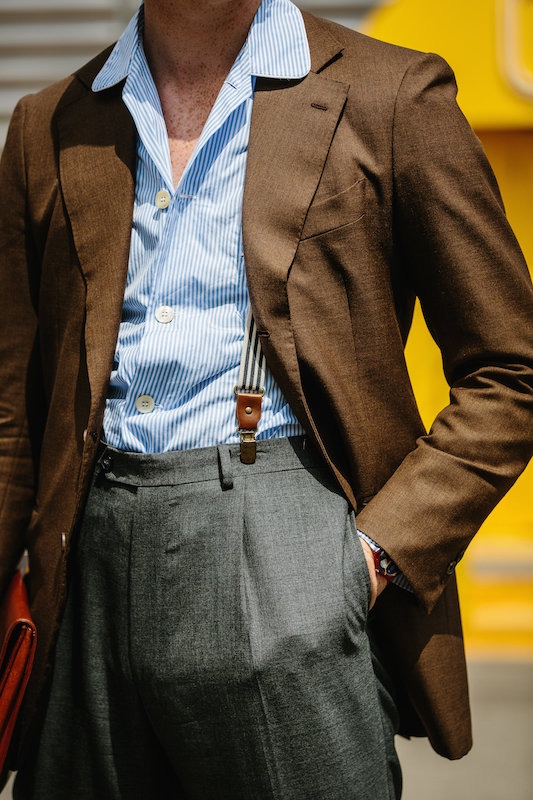 Clip-on braces worn with high-waisted, pleated trousers. Up top, the striped, camp collar shirt wears well over the brown blazer.