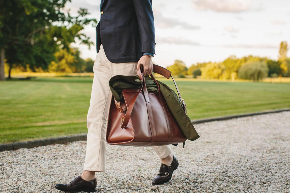 The Rake's Ben St George wearing a Sciamat blazer, Carmina cordovan monk straps and carrying a Grenfell Shooter jacket and a Frank Clegg signature leather travel duffle.