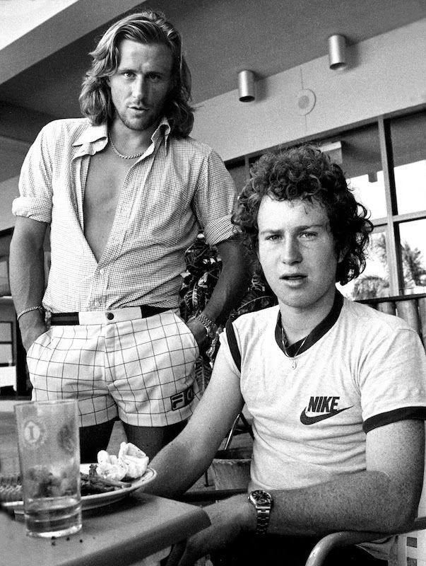 1970s pin-ups Bjorn Borg and John McEnroe's long hair and louche style epitomised their rebellious streaks and bohemian nature. Borg wears Fila shorts and an unbuttoned shirt tucked in, and McEnroe wears a Nike T-shirt with one sleeve casually rolled up.