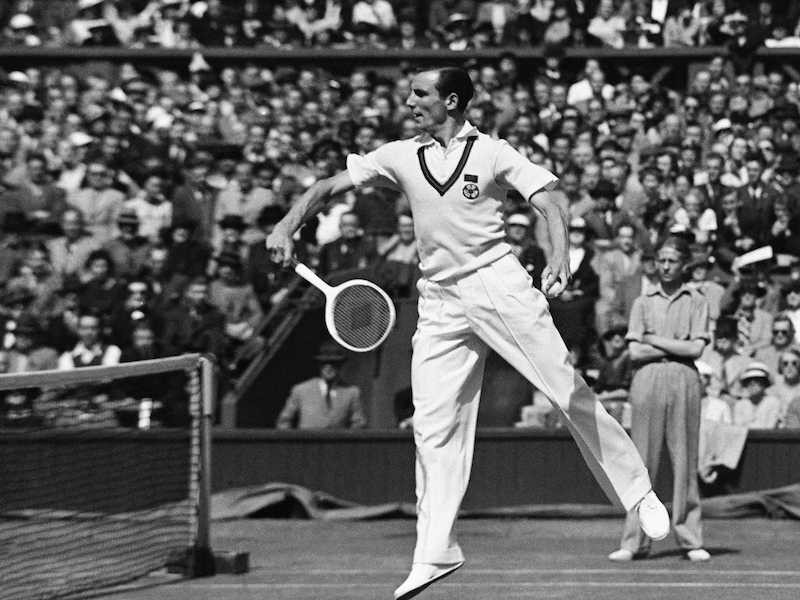 The stylish Fred Perry in a white sweater vest and with perfectly parted hair, playing at Wimbledon, 1936.