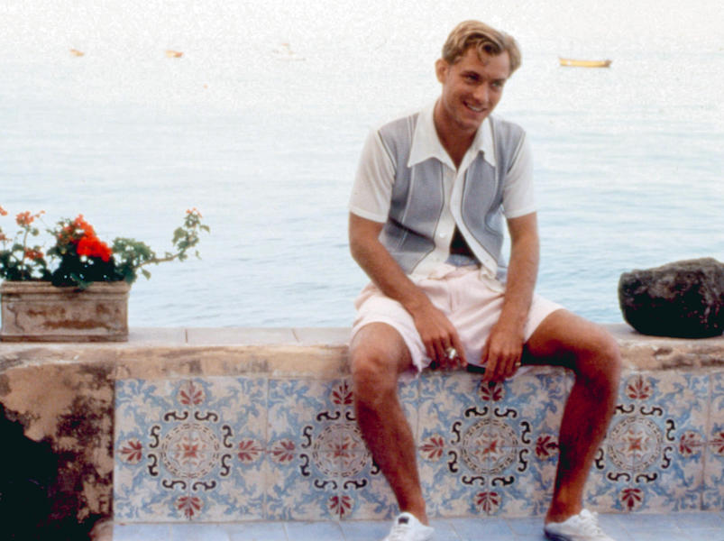 Jude Law wears a pointed collar shirt fastened only at the second button down, over pale pink shorts and slipped-on plimsolls in the role of Dickie Greenleaf. Paramount Pictures/ Courtesy: Everett Collection.