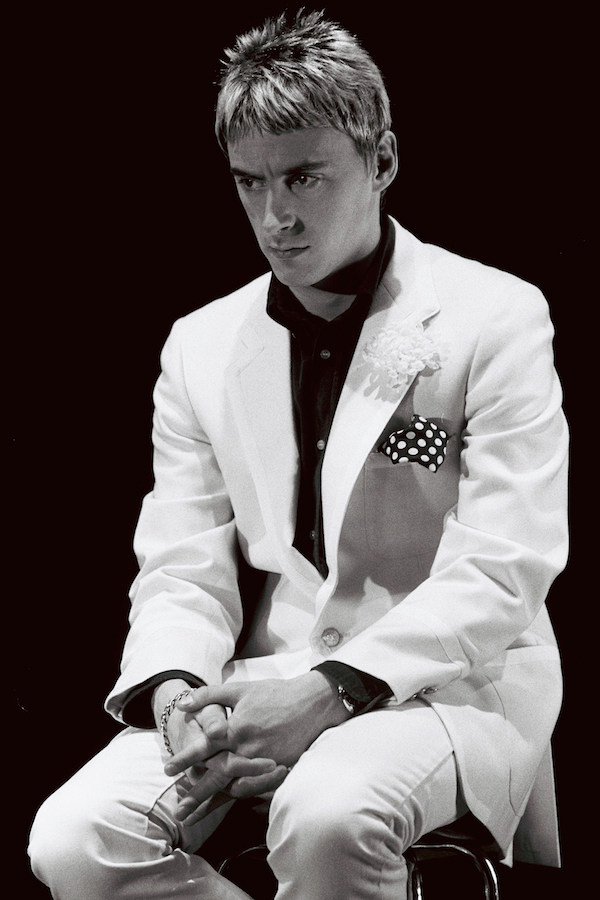 Paul Weller pairs a white suit with a spotted pocket square and dark buttoned-up shirt in 1985. Photo by Clare Muller/Redferns/Getty Images.