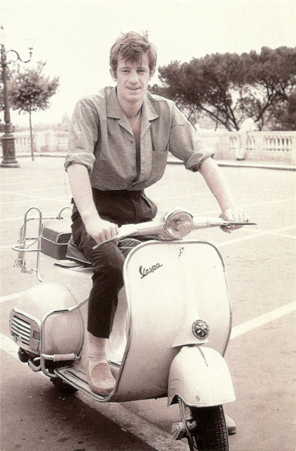 Jean-Paul Belmondo displaying his Riviera credentials with high-waisted, pleated trousers, a tucked in camp collar shirt, loafers and a Vespa, circa 1960s.