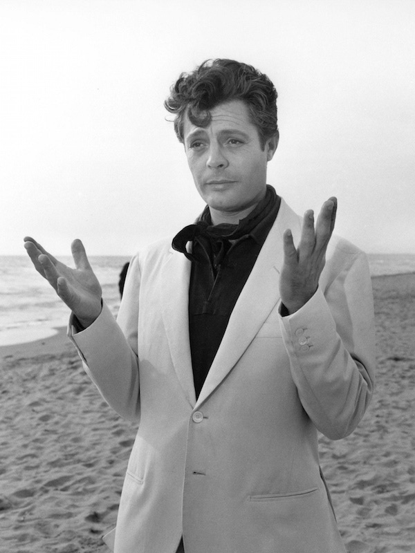 Marcello Mastroianni embodied Riviera style in 1960's La Dolce Vita, here pictured on the beach with a white suit, black shirt and neckerchief combination.