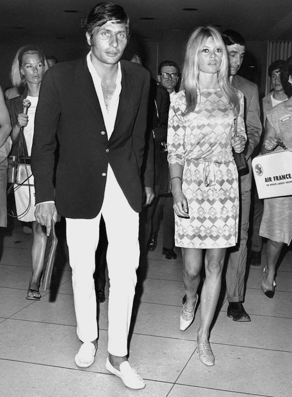 A quintessential Riviera look by Gunter Sachs, featuring his signature white trousers, a low-buttoned shirt, a soft, dark blazer and white loafers. He’s pictured with Brigitte Bardot, circa 1960s.