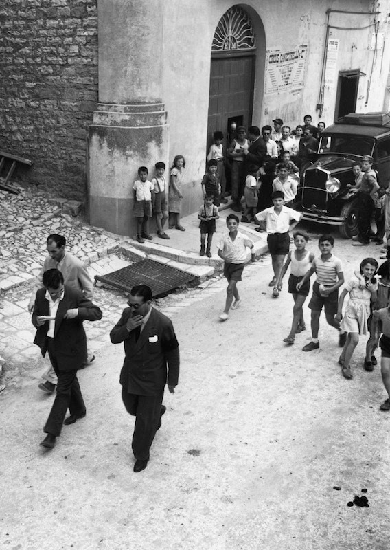 Exiled Mafia boss Charles 'Lucky' Luciano and entourage draw a crowd, mainly of children, as they walk down a street in Sicily, 1949. Photo by Slim Aarons/Getty Images.