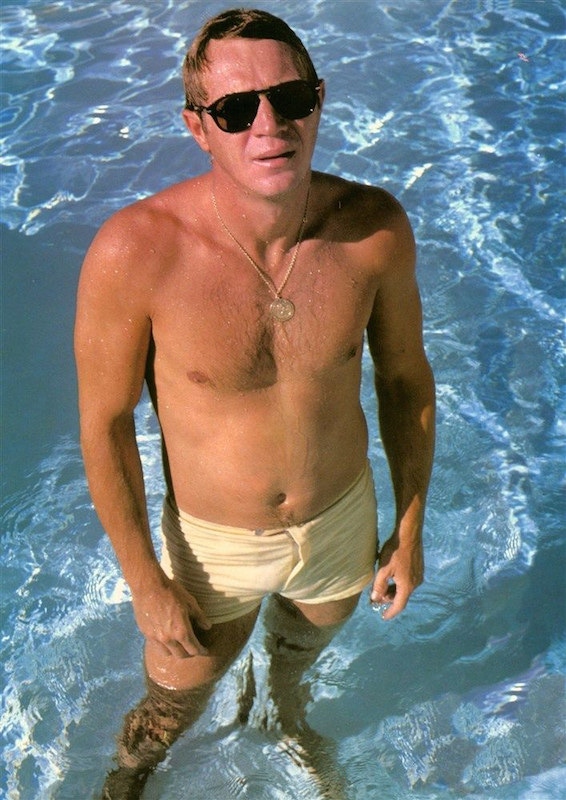 Steve McQueen wearing swim shorts and his signature Persol sunglasses, circa 1960s.