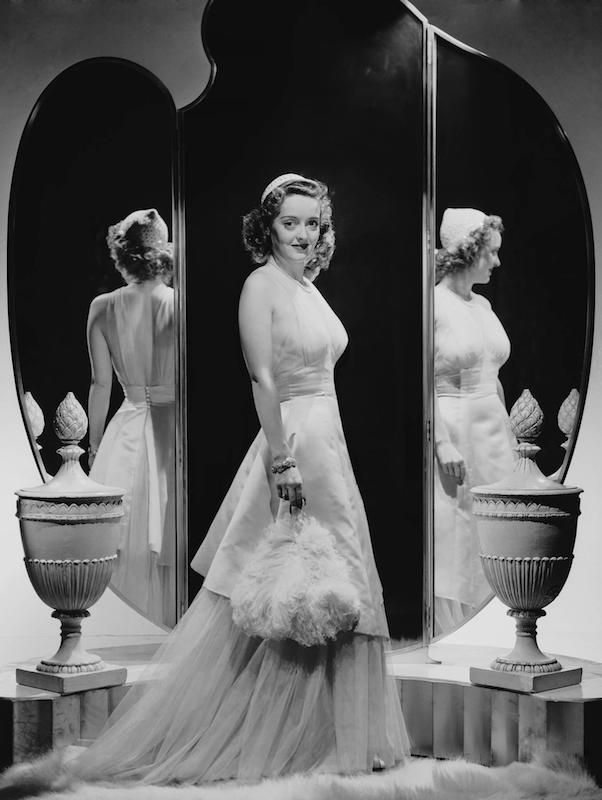 Three shades of Bette: posing in front of an elaborate mirror, circa 1930s.