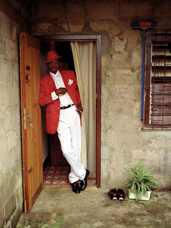 The sapeur Delagrace, also known as the Icon of Beautiful Colours, in the doorway of his rented room.