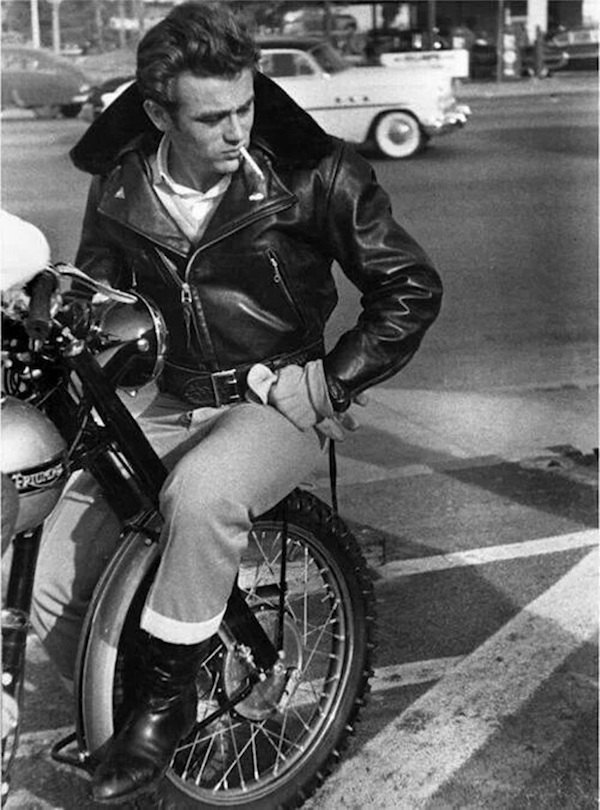 Wearing his leather biker jacket whilst sitting on the front tyre of his Triumph, circa 1955.