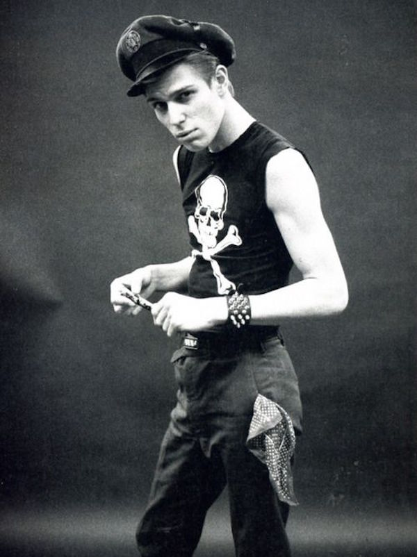 Wearing a military hat, skull and crossbones sleeveless vest, studded wristband and black jeans with a nonchalant bandanna hanging out of the pocket, 1976. Photograph by Pennie Smith.