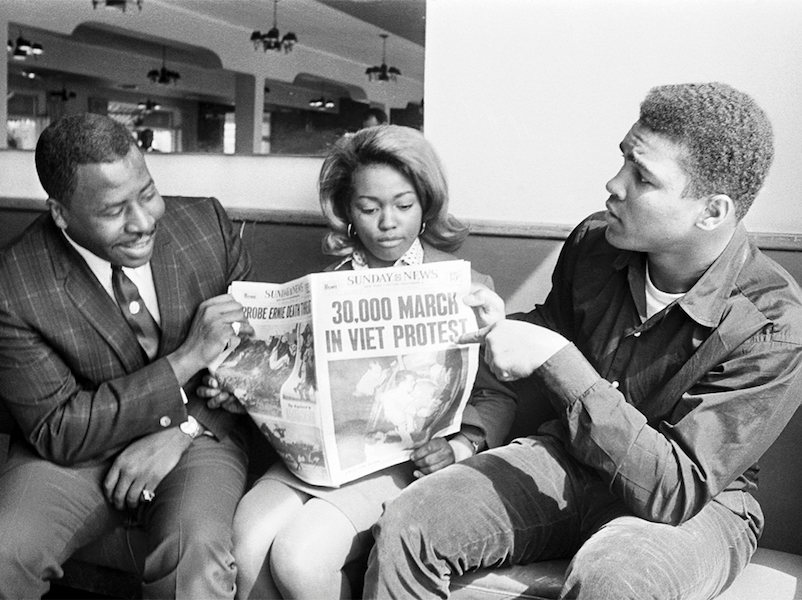 Boxing champion Muhammad Ali refused to be inducted into the U.S. Army and was immediately stripped of his heavyweight title. Here, he can be seen passionately discussing a newspaper with the headline, '30,000 march in Viet Protest', in 1967.