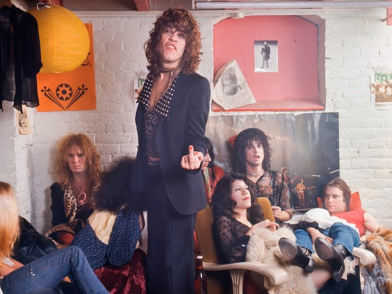 The New York Dolls relax in their dressing room at Paradiso in Amsterdam while David Johansen puts a middle finger up to the camera, 1973. Photo by Gijsbert Hanekroot/Redferns/ Getty Images.