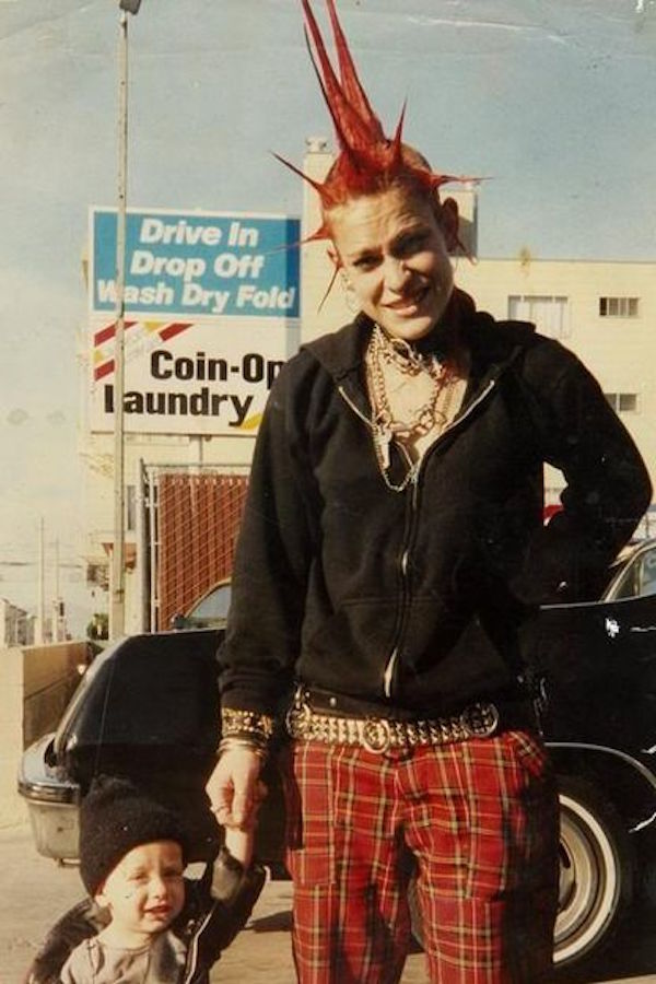 A punk in the USA wears tartan trousers and a black jacket, studded belt and layers of chain jewellery. The spiked mohican hair do is emblematic of non-conformity, dyed the same colour as the trousers.