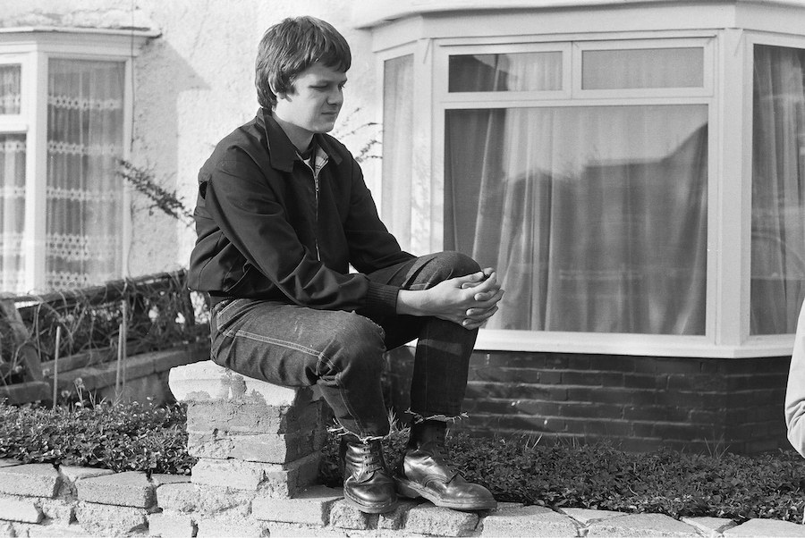 A British teenager wearing frayed denim jeans, heavy work boots and a Harrington jacket - the uniform of the skinhead - in 1980. Photo by Mark Charnock/PYMCA/REX/Shutterstock.