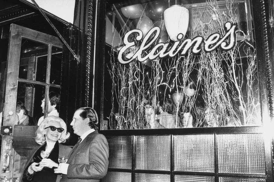 Two guests stand outside the window of Elaine’s restaurant in Manhattan, New York. Photo by Robin Platzer/Twin Images/The LIFE Images Collection/Getty Images.