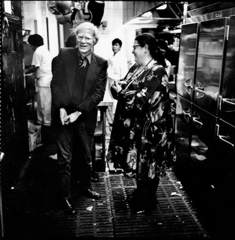 Andy Warhol and Elaine share a joke in the kitchen of Elaine's, circa 1979.