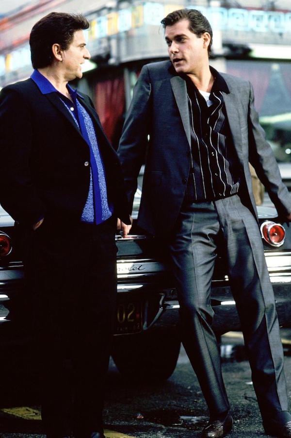 Liotta (right) wears a grey charcoal suit over a button-through knitted polo, alligator skin tassel loafers and a white vest. Joe Pesci wears a similar look, with a dark suit and blue shirt.