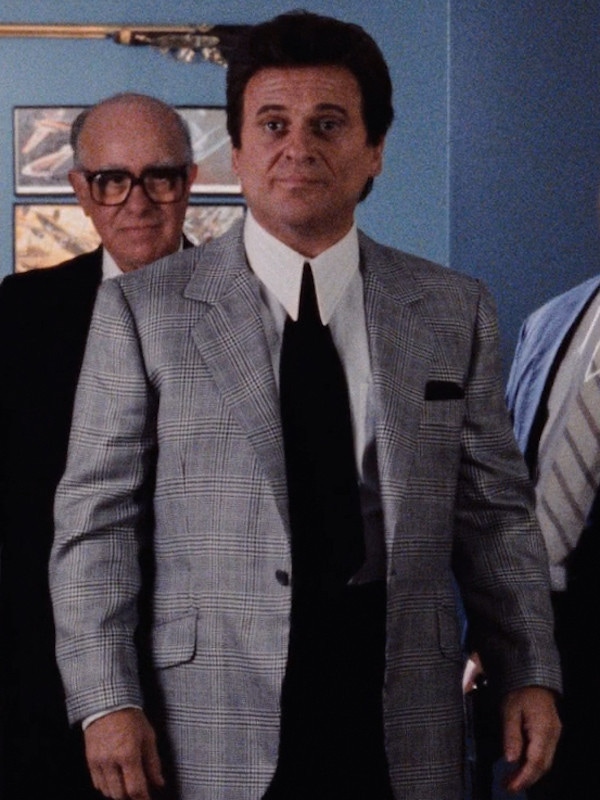 Tommy, played by Joe Pesci, wears a tonal grey unbuttoned glen-check jacket with notch lapels, slanted flap pockets and narrow turn-up cuffs. In his breast pocket, he wears a black pocket square to match his wide, black tie and contrast his crisp white collar and cuffs.