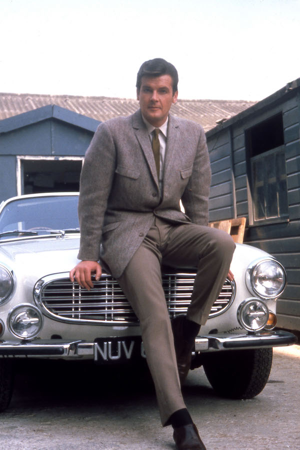 Roger Moore leans against his Volvo car while filming the TV series The Saint at Elstree Studios in North London, 1967. Photo by Pictorial Press Ltd/Alamy Stock Photo.