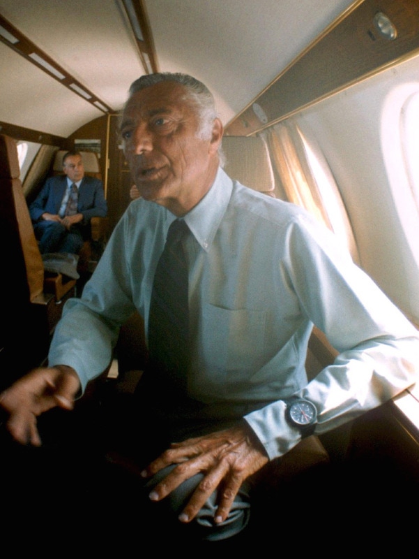 Gianni Agnelli wearing a light blue button-down shirt with his watch worn over the cuff on a private plane in 1975.