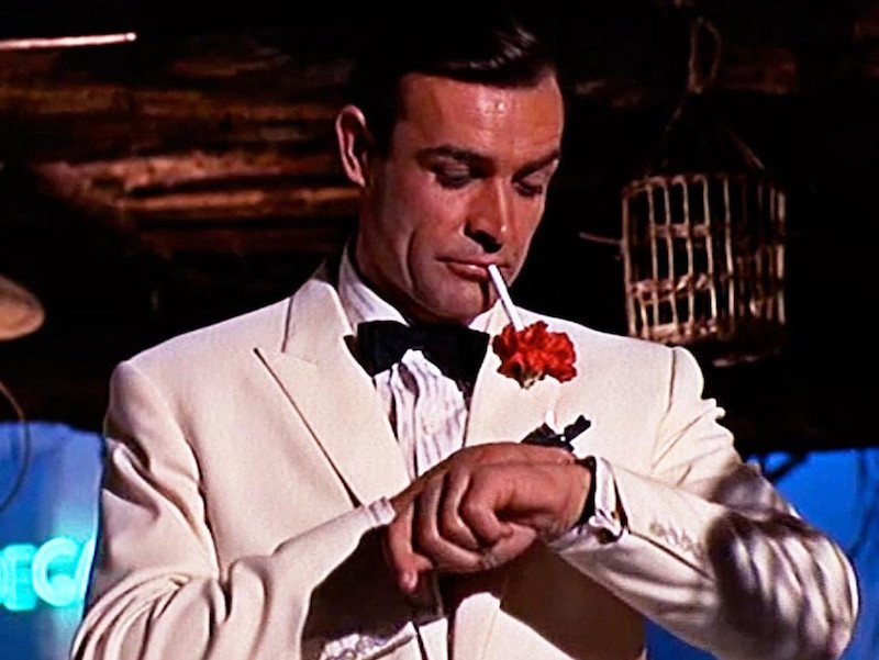 Sean Connery checking the time on his Rolex Submariner ref. 6538, paired with one of the most rakish white dinner jackets in cinema in Goldfinger, 1964.