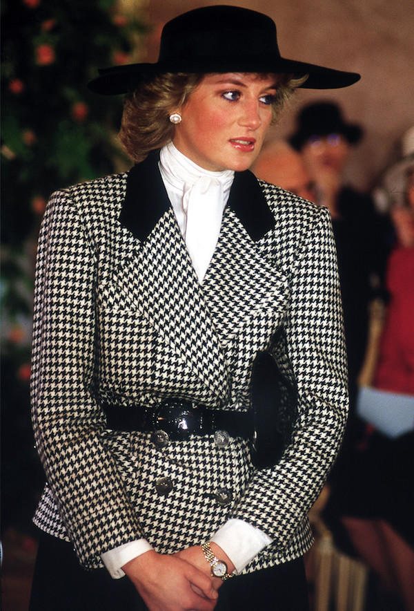 In 1987 on a German tour, Diana wears a conservative houndstooth jacket with black collar designed by Alistair Blair, with a hat by milliner Philip Somerville, and her signature pearl earrings.