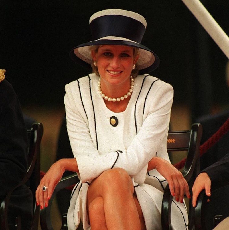 In a white two-piece with an elegant black trim, oversized pearls, and matching millinery at VJ Day celebrations, 1995. On her left hand is the engagement ring given to her by Prince Charles, made by Garrard & Co.