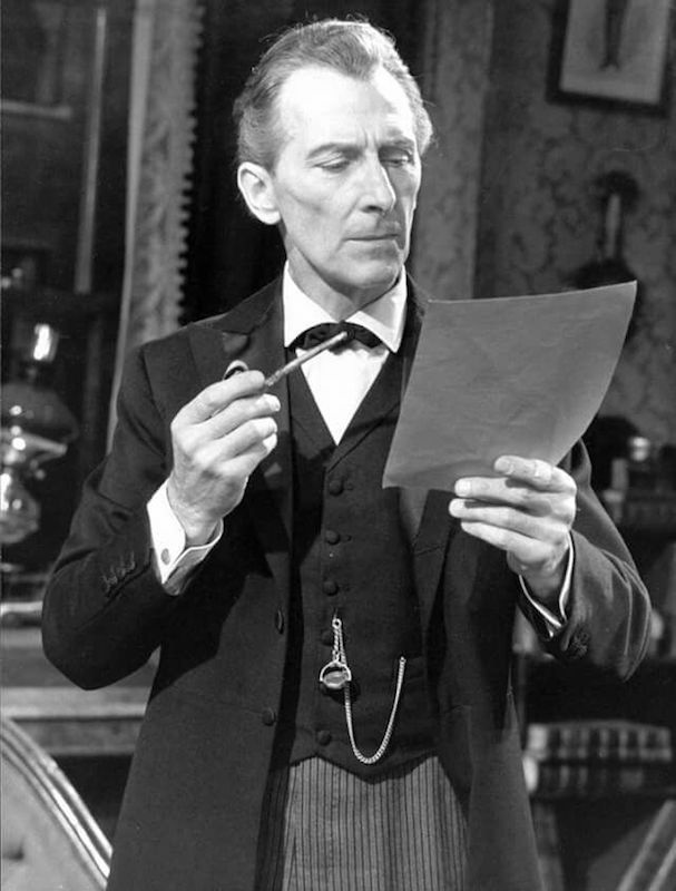 Peter Cushing in the 1968 series of Sherlock Holmes, smoking a pipe while reading. Sherlock's style over the years has paralleled the decline of formal dress, as seen here; Cushing wears double-cuffs, a waistcoat and a pocket watch.