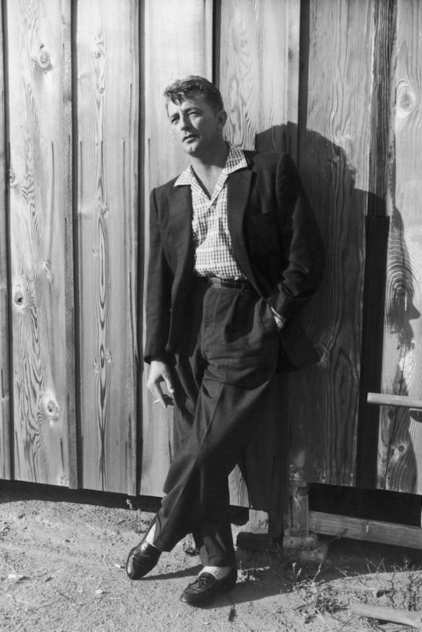 Robert Mitchum wears wide-legged trousers and a full cut jacket, with a cuban-collar shirt underneath, circa 1940s.