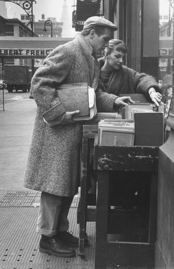 Paul Newman browses a bookstore with Joanne Woodward, wearing turn-up trousers, worker boots and a full-length overcoat. Photo by Gordon Parks/Time Life Pictures/Getty Images.