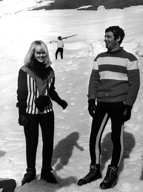 Jean-Paul Belmondo is the epitome of cool casual in a striped knitted jumper, ski leggings and lace-up snow boots with actress Mylene Demongeot in Megève, France, 1966.