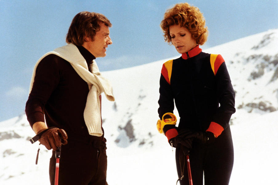 Former French ski champion Jean-Claude Killy layers his knitwear with a white jumper perfectly folded over his shoulders. He is pictured here with fellow actress Daniele Gaubert on the set Snow Job, 1972. Photo by Jacques Dejean/Sygma via Getty Images.