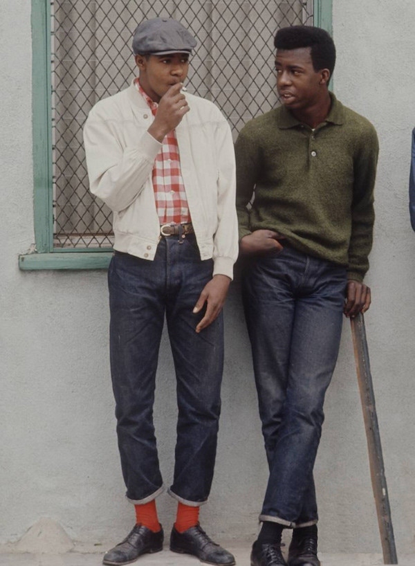 Preppy rebels from Los Angeles' Watts community purposefully dressed well to diffuse racial stereotyping in the 1960s. Here, one wears a peaked cap with a casual, considered look that includes an off-white blouson and turn-up jeans.