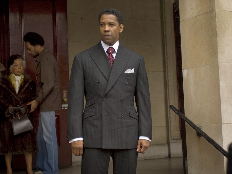 This is Lucas’ most formal business look in the film which he wears before being arrested. The dark grey double-breasted pinstripe suit features a 6x2 button stance (the lower button left undone) and angular flap pockets, worn with a three-pointed silk pocket square, a burgundy and navy striped tie with yellow polkadots and a crisp white pointed collar shirt. The look is more Wall Street banker than heroin trafficking kingpin, but it works.